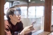窓辺でスマートフォンを持つ男性