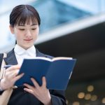 ビルの外で手帳を開きスケジュールを確認する学生