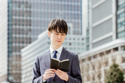 ビルの外で手帳を開きスケジュールを確認する学生