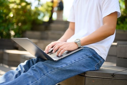 屋外で座りながらパソコンを操作する学生